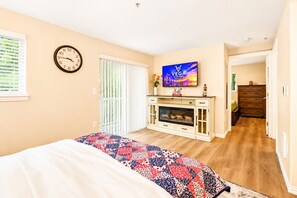 A bedroom with a bed, a TV on the wall, a clock, and a sliding door leading to another room. - Vega Apartment Seattle (Seattle)