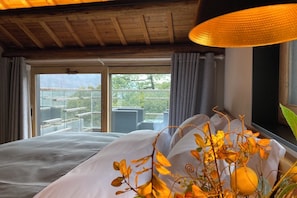 Hotellihuone, jossa on sänky, ikkuna verhoilla, näkymä ulos ja riippuvalaisin.