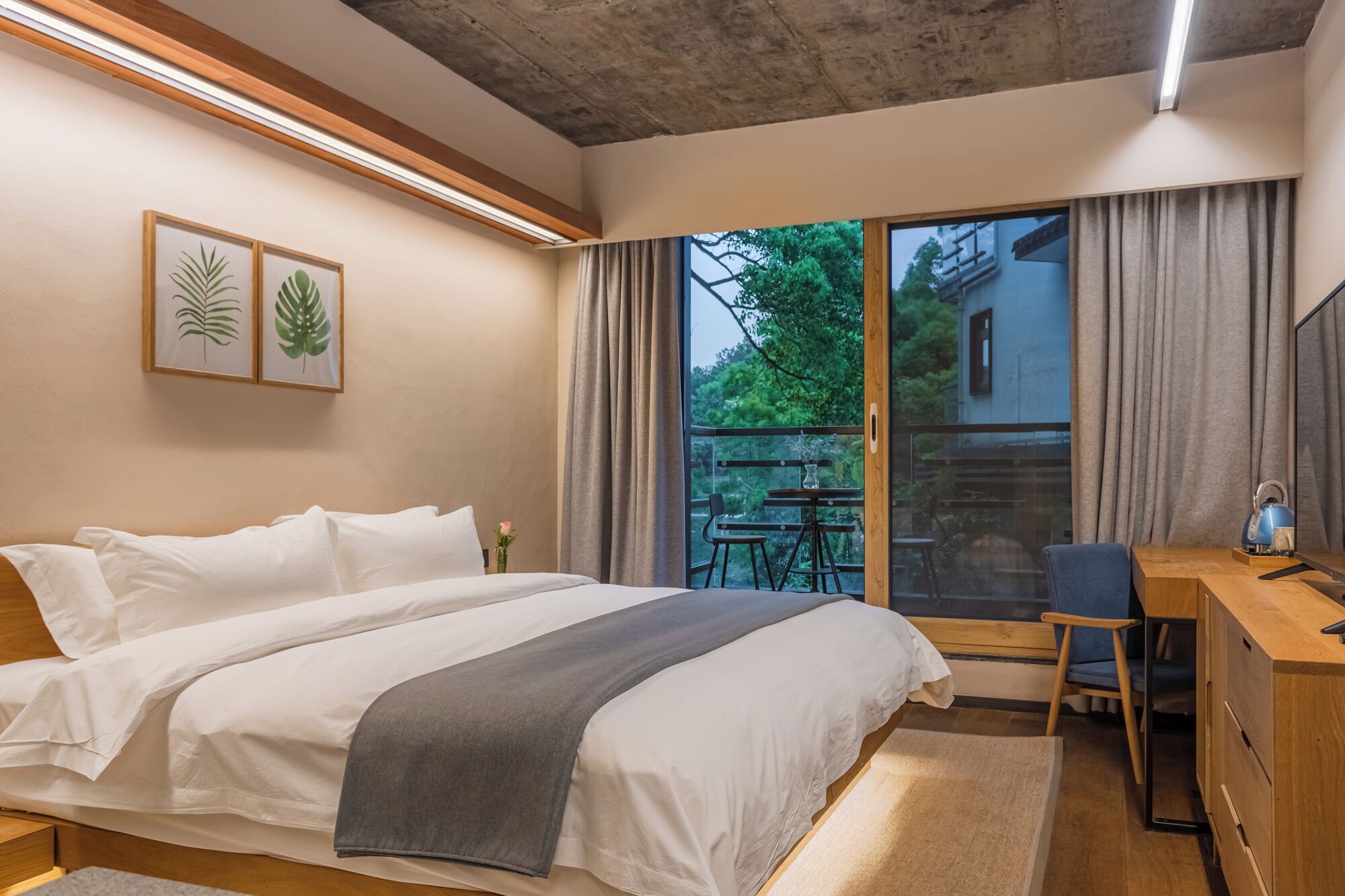 A bedroom with a bed, a desk, a chair, and a view of the outdoors.