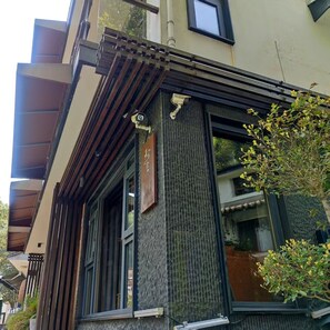 A building with a wooden facade, a window with a view, and a small tree. - WuTiaXinShe Guesthouse West Lake Branch (Hangzhou)