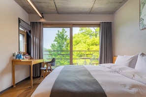 Hotellihuone, jossa on sänky, työpöytä, tuoli ja suuri ikkuna, josta on näkymä puita kohti.