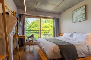 Hotellihuone, jossa on sänky, työpöytä, tuoli ja suuri ikkuna, josta on näkymä puita kohti.