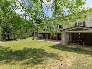 Ein Steinhaus mit überdachter Terrasse, Gartenmöbeln und einem Rasen.