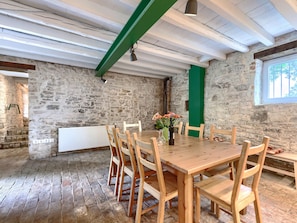 Une salle à manger rustique avec une table et des chaises en bois, des murs en pierre et une poutre verte.