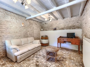 A room with a stone wall, a white sofa, a wicker chair, a wooden desk with a TV, and a barrel. - Villa Krase by Interhome (Svetvinčenat)
