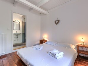 Ein Schlafzimmer mit einem Bett, zwei Nachttischen mit Lampen, einer herzförmigen Dekoration an der Wand und einem Badezimmer mit Spiegel und Waschbecken.