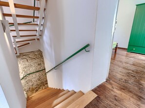 Eine Holztreppe mit grüner Handläufe führt zu einem Raum mit einer Steinwand und einem grünen Schrank.
