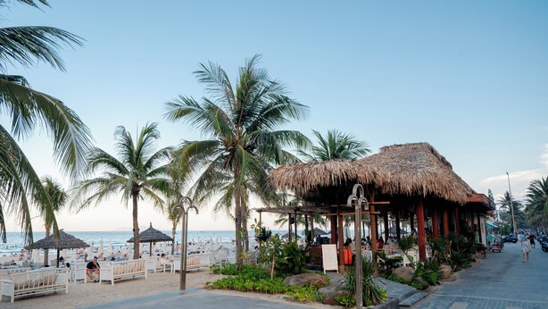 A beachside restaurant with outdoor seating, palm trees, and a thatched roof structure. - Nani's Hotel & Apartment (Da Nang)