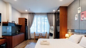 A hotel room with a bed, a desk with a sink, a chair, a TV, and a window with curtains. - Nani's Hotel & Apartment (Da Nang)
