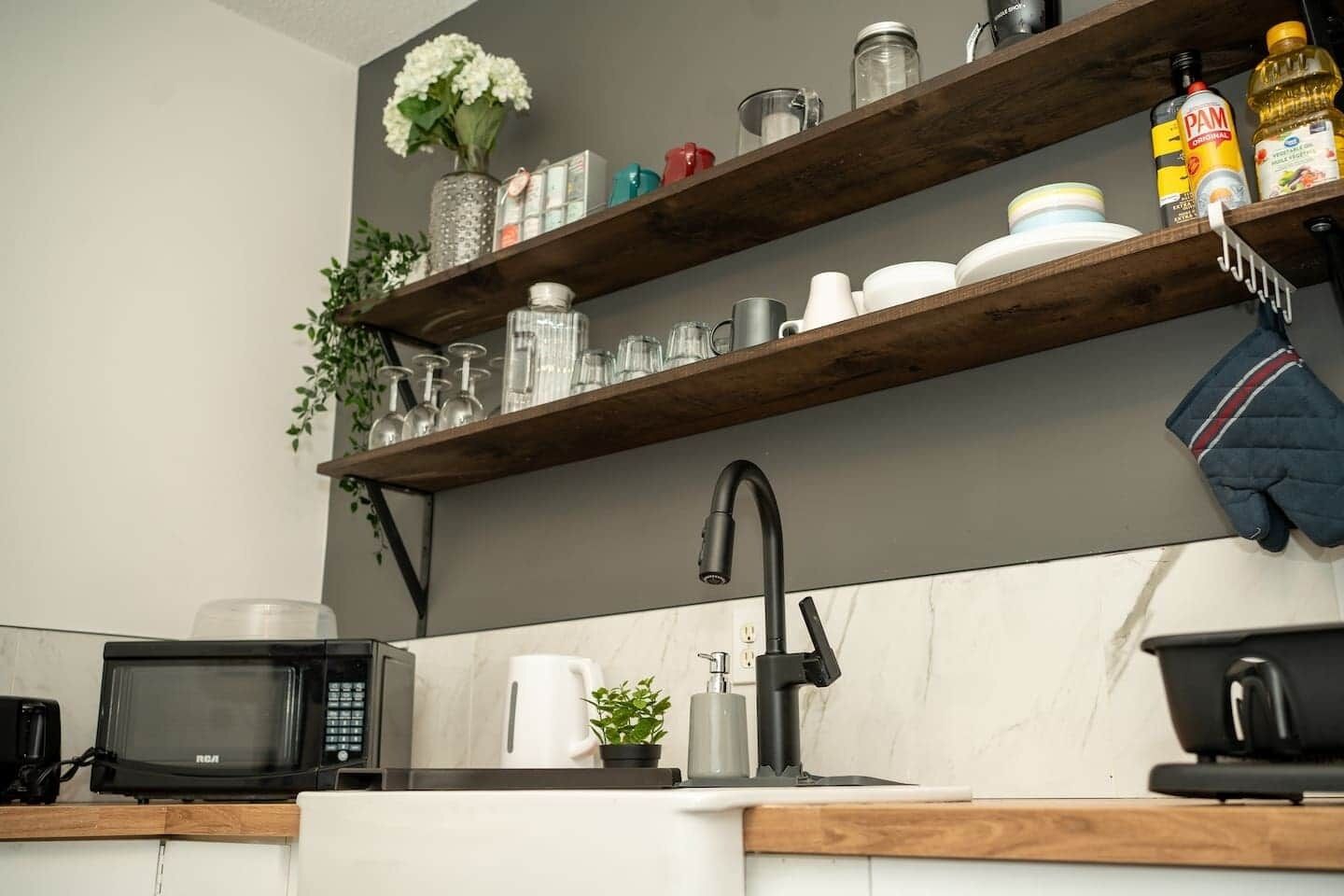 A kitchen with a microwave, sink, and shelves holding various kitchen items.