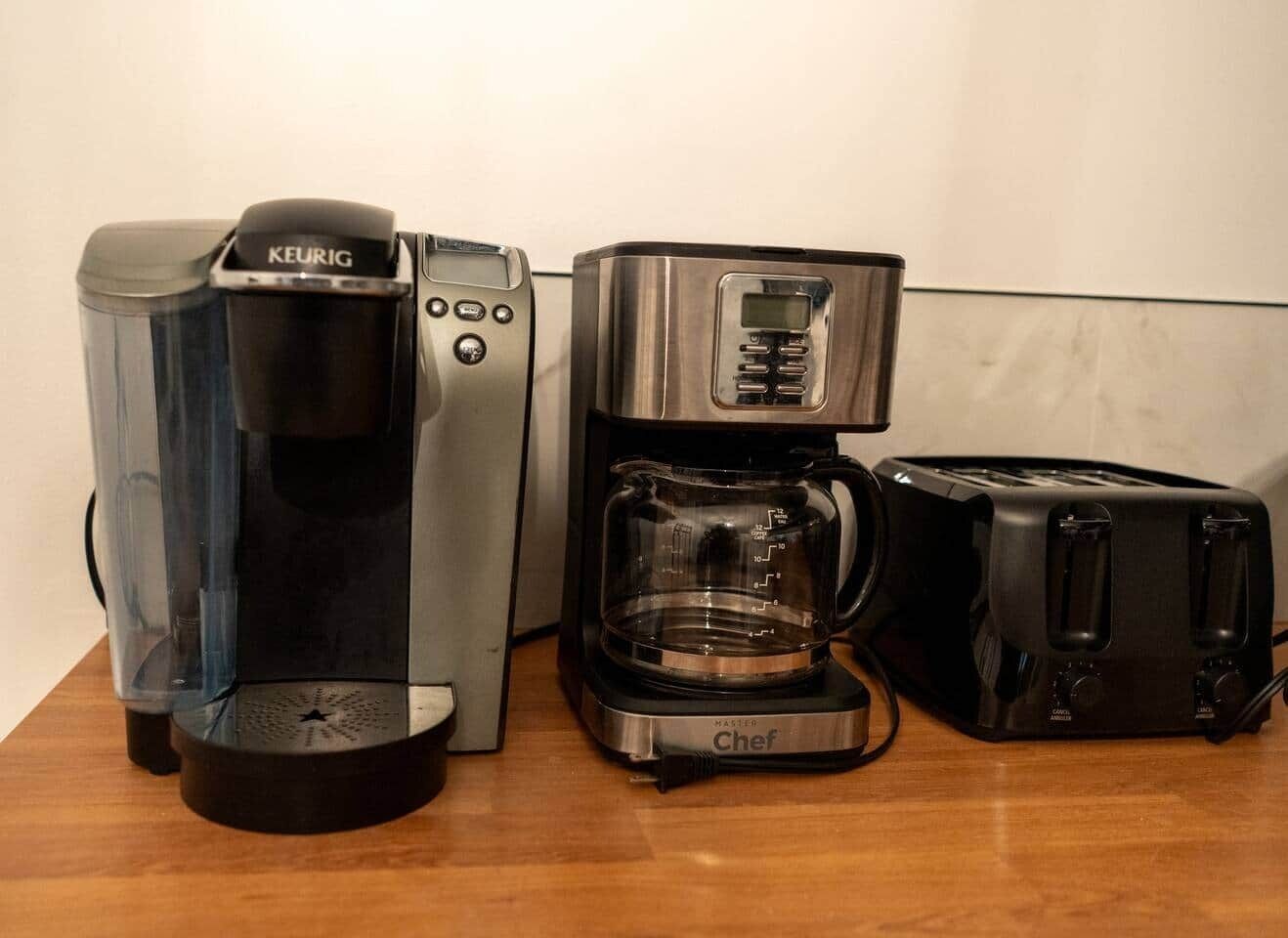Una moka, una caffettiera e un tostapane su un ripiano di legno.