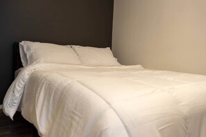 Un letto rifatto con biancheria bianca in una stanza con una parete scura e un pavimento chiaro.
