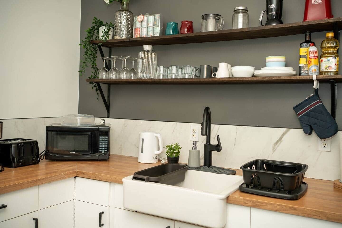 A kitchen with a microwave, toaster, sink, and shelves with glassware and kitchen items.