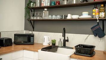 A kitchen with a microwave, toaster, sink, and shelves with glassware and kitchen items.