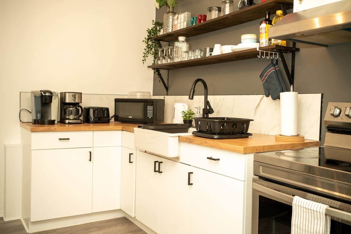 A modern kitchen with white cabinets, a microwave, coffee maker, and a stove.