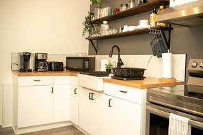Una cuina moderna amb armaris blancs, un microones, una cafetera i una placa de cocció.