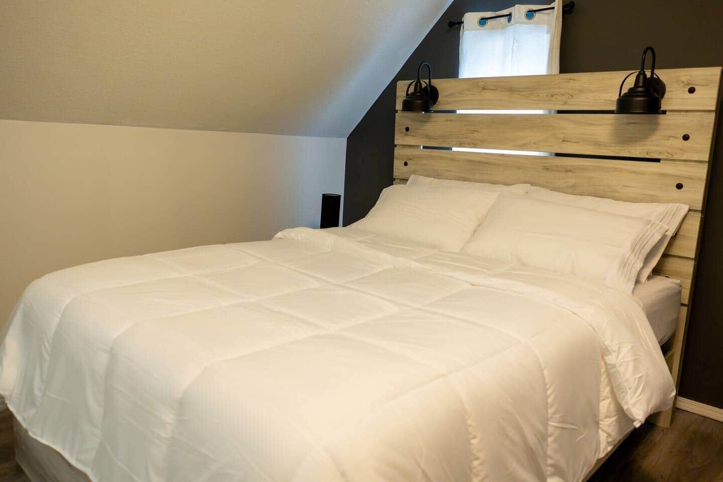 A bed with a wooden headboard, white bedding, and a nightstand with a lamp.