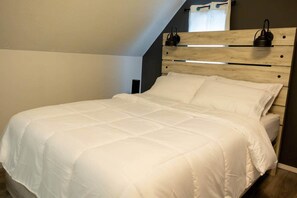 A bed with a wooden headboard, white bedding, and a nightstand with a lamp. - Cozy 2Br Home near Downtown WPG | Free Parking (Winnipeg)