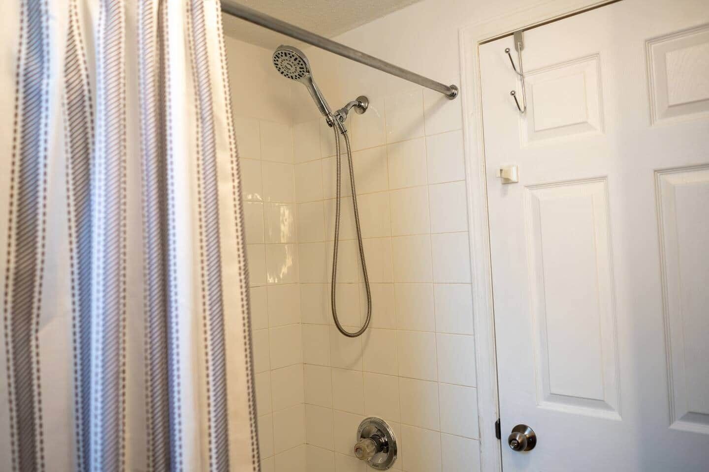 A shower with a handheld showerhead, a grab bar, and a door with a handle.