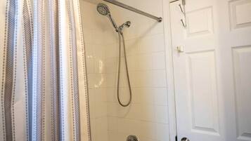 A shower with a handheld showerhead, a grab bar, and a door with a handle.