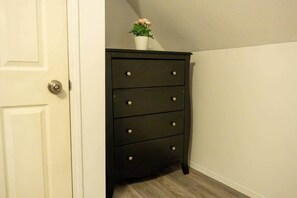 A dark wooden dresser with four drawers and a small potted plant on top, positioned against a white wall with a door to the left. - Cozy 2Br Home near Downtown WPG | Free Parking (Winnipeg)