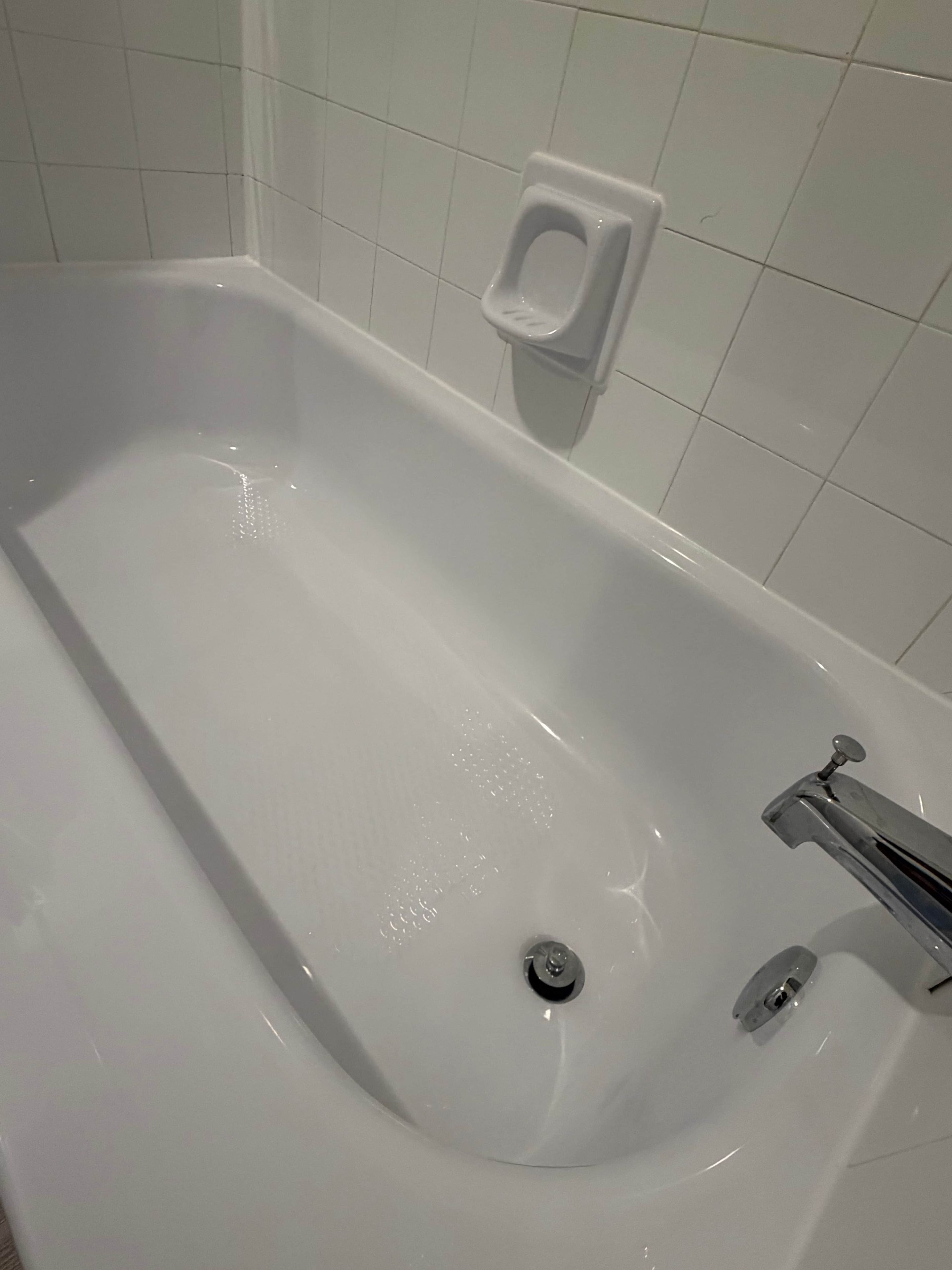 Eine weiße Badewanne mit einem chromfarbenen Wasserhahn und einer Seifenschale an der Wand.