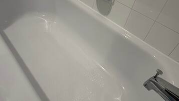 Una vasca da bagno bianca con un rubinetto cromato e un portasapone a parete.