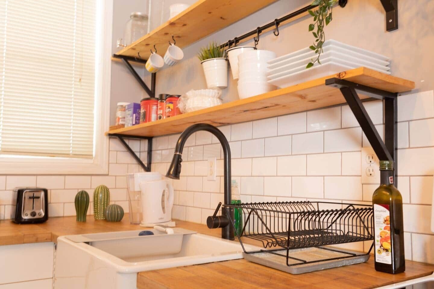 A kitchen with a wooden shelf, a black faucet, a sink, and a bottle of olive oil.