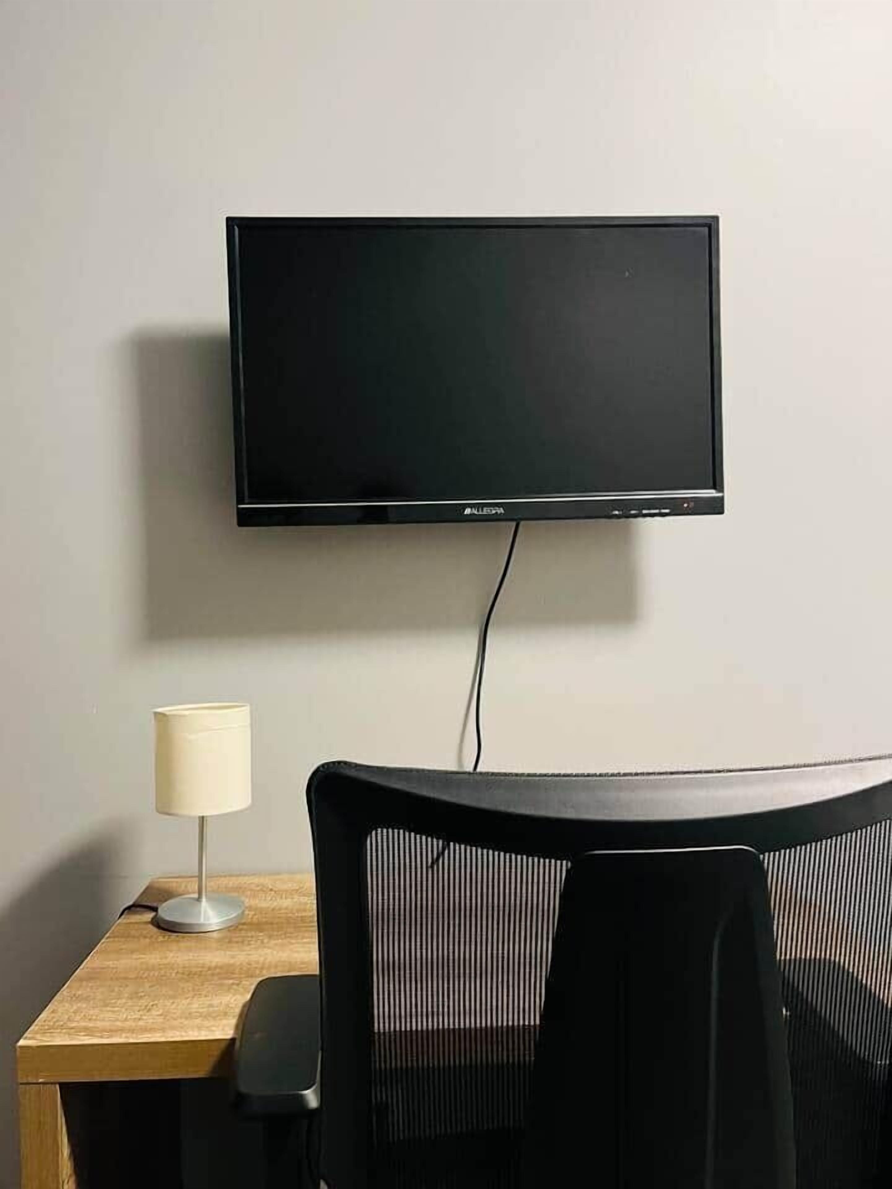 Un téléviseur à écran plat fixé au mur, un bureau avec une lampe et une chaise.