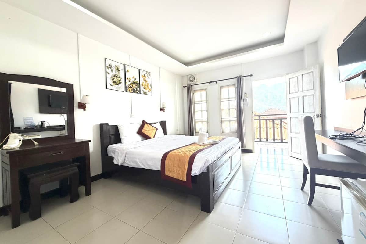 A hotel room with a bed, desk, chair, and a balcony with a view.