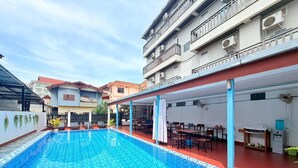 A swimming pool with tiled flooring, outdoor seating, and a covered area with tables and chairs. - Cozy Corner Hotel (Vang Vieng)