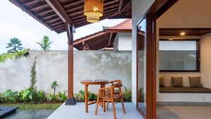 Un espacio al aire libre techado con mesa y sillas, una lámpara colgante y vistas a la vegetación circundante.