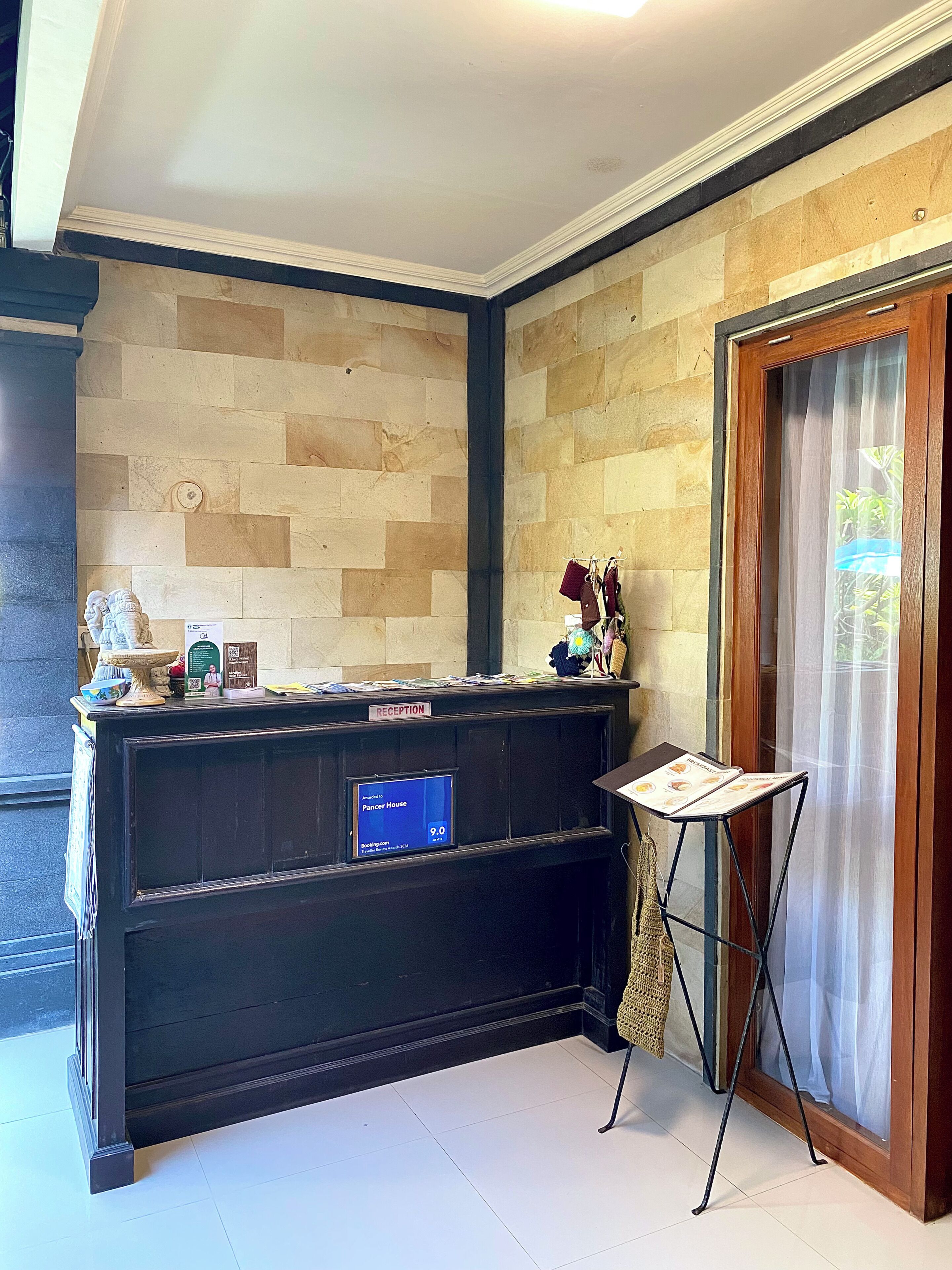 A reception desk with a sign indicating 'Reception,' a digital display, and a window with a curtain.