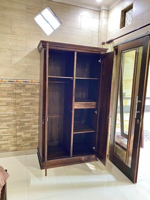 A room with a large wooden wardrobe, a tiled floor, and a stone wall. - Pancer House (Ubud)
