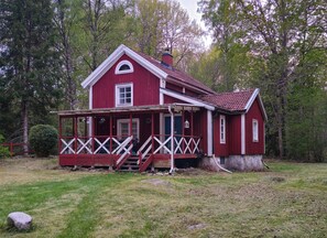 Una casa di legno rossa con un portico, un camino e un piccolo giardino.