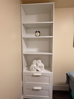 A white wardrobe with shelves, a clock, and rolled towels.