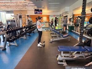 Un gimnasio con equipo de levantamiento de pesas, bancos y una pantalla de televisión.