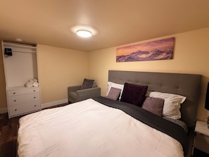 A bedroom with a bed, a nightstand, a dresser, a chair, a painting, and a ceiling light.