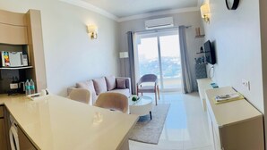 A modern hotel room with a dining area, a sofa, a TV, and a view of the city through the window. - Aravali Hill CherisingBeauty 1BHK CP3Flower Valley (Gurugram)