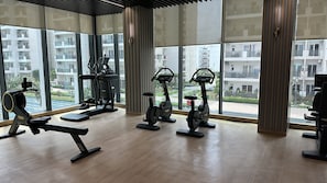 Ein Fitnessstudio mit unterschiedlichen Trainingsgeräten, großen Fenstern und Blick auf Wohnhäuser.