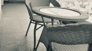 A balcony with wicker chairs and a round table, a speaker mounted on the wall, and a cityscape view. - Aravali Hill CherisingBeauty 1BHK CP3Flower Valley (Gurugram)