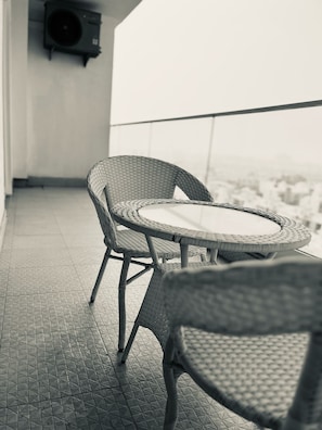 Ein Balkon mit Korbstühlen und einem runden Tisch, ein an der Wand befestigter Lautsprecher und Blick auf die Stadtlandschaft.