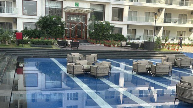 A hotel with a swimming pool, outdoor seating, and a well-maintained garden. - Aravali Hill CherisingBeauty 1BHK CP3Flower Valley (Gurugram)