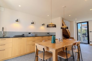 A modern kitchen with wooden cabinets, a dining table, and pendant lighting.