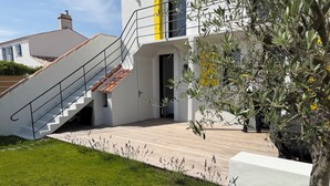 Una casa moderna con fachada blanca, terraza de madera y una escalera que lleva a una puerta amarilla.