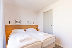 A hotel room with two beds, a wooden headboard, a wardrobe, and two framed pictures on the wall.