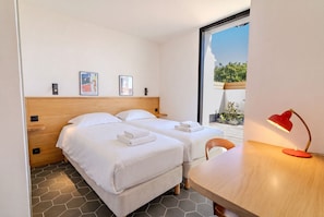 Ein Hotelzimmer mit zwei Betten, einem hölzernen Kopfteil, einem Schreibtisch mit roter Lampe und einem großen Fenster.
