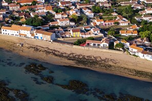 Vue aérienne d’une ville côtière avec des bâtiments blancs, une plage de sable et des affleurements rocheux.
