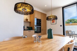 Een moderne keuken met houten keukenkastjes, een inbouwoven en een eethoek met een houten tafel en stoelen.