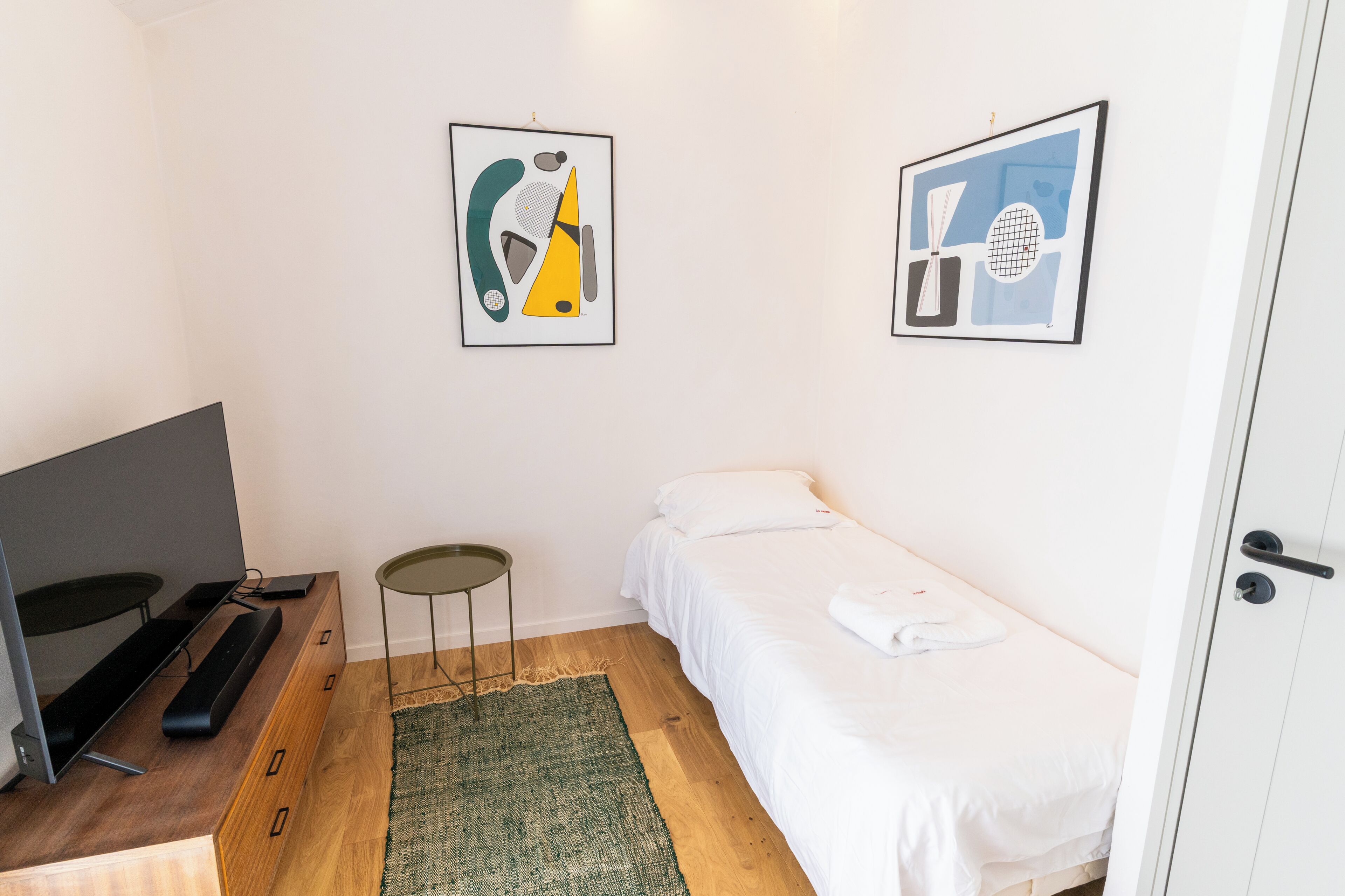 Une chambre d’hôtel comprenant un lit, un bureau avec un ordinateur, une petite table et deux œuvres d’art abstraites accrochées au mur.